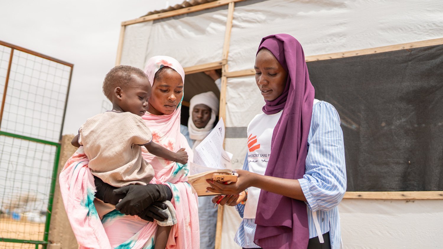MSF worker showing a form to a woman holding a child