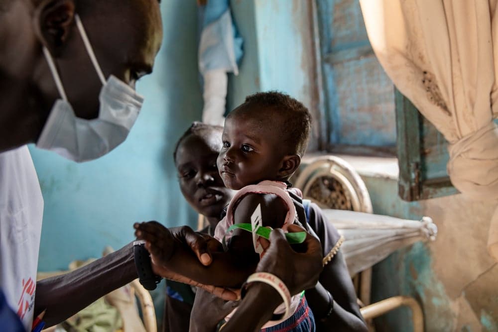 Mother holds her baby as a member of Doctors Without Borders/ Médecins Sans Frontières staff measures the child’s level of nutrition. Image is from South Sudan.